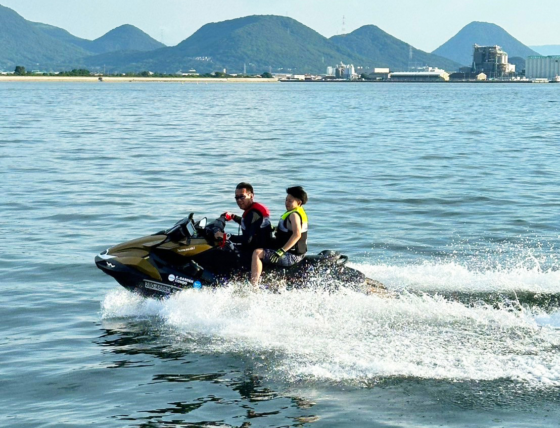 山並みを背景に、水上バイクでツーリングを楽しむ2人。水しぶきを上げながら滑走中