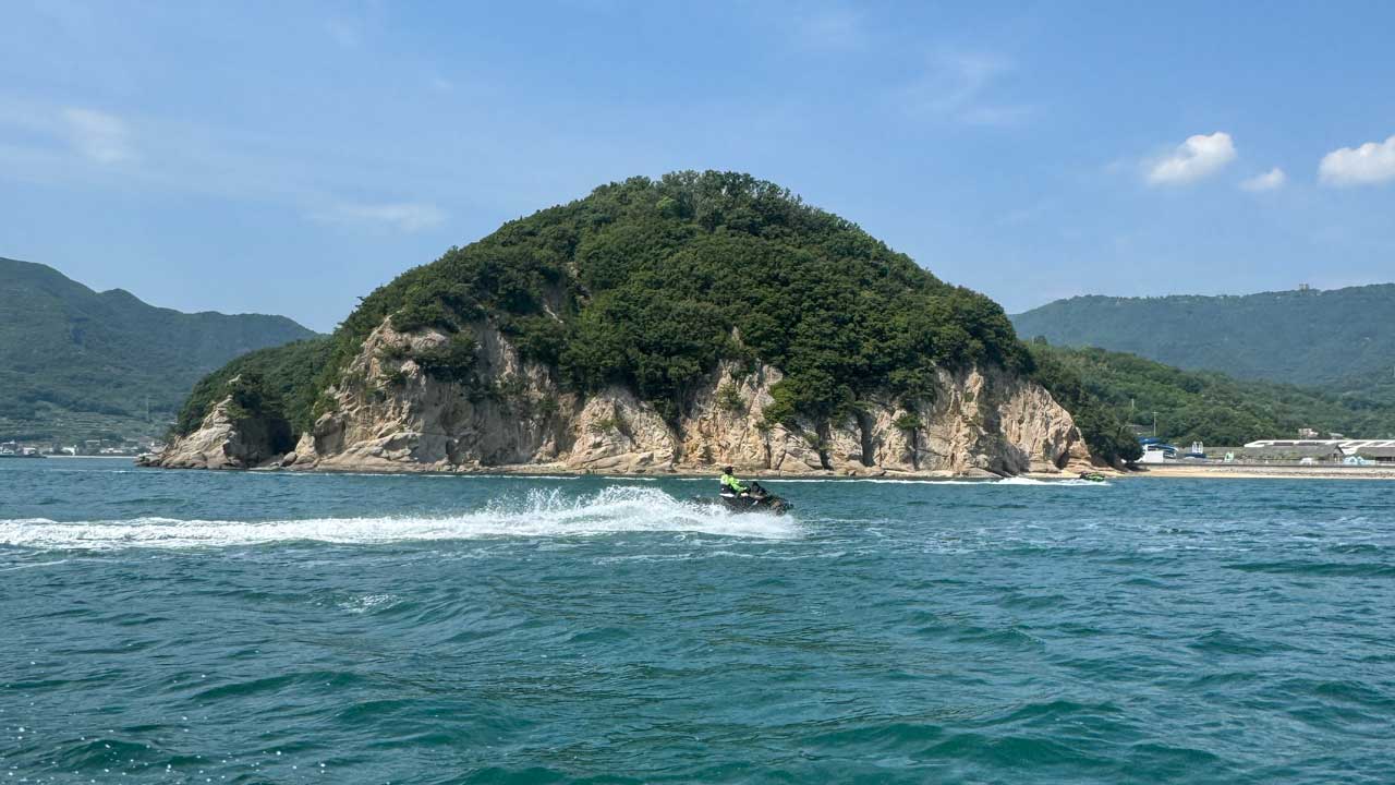 緑豊かな島を背景に、海上を水上バイクで走る女性