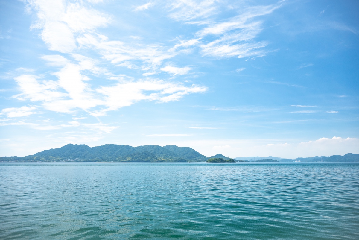 青空の下、穏やかな海と山々が広がる風景